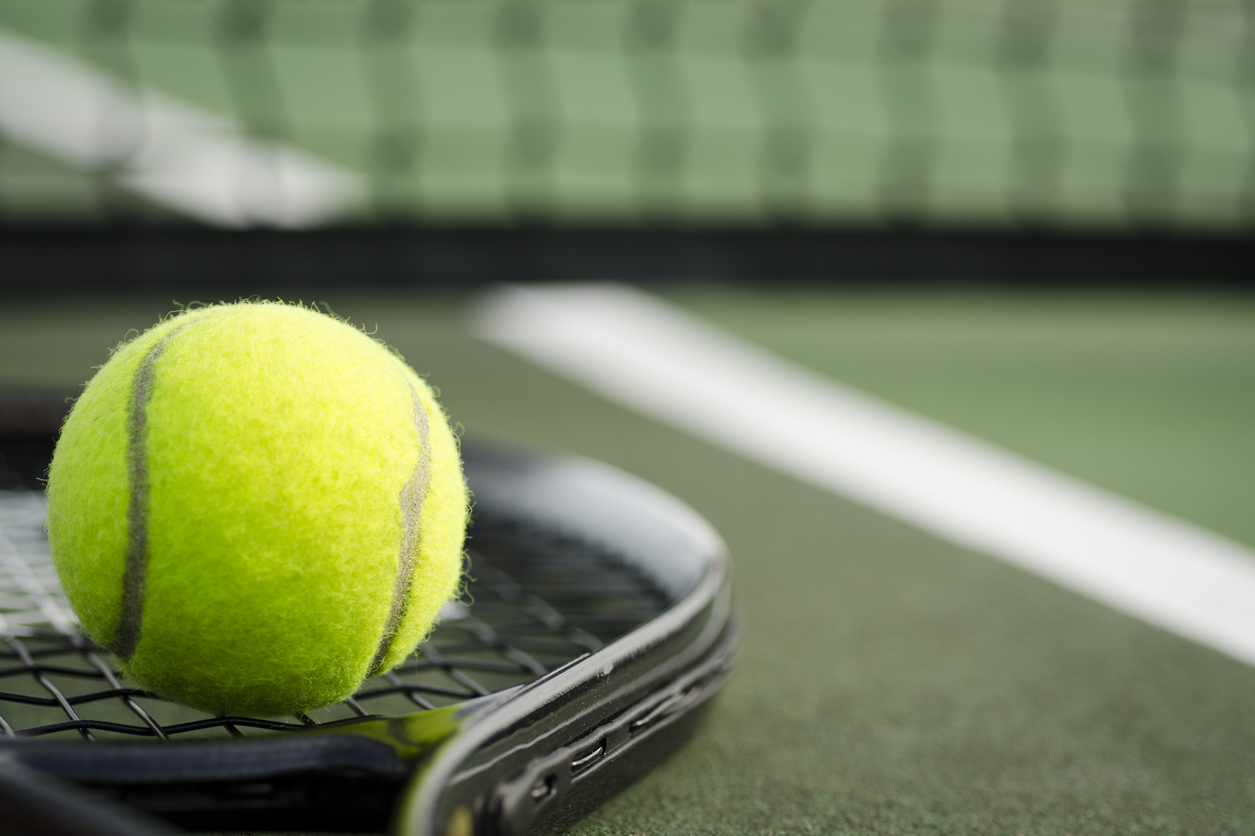 tennis ball balanced on a tennis racket in front of a tennis net